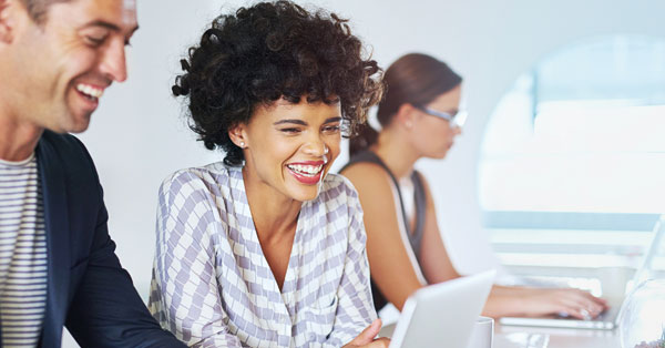 Two people sitting together, smiling while looking at a laptop, as they search for job vacancies