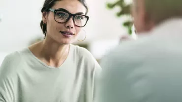 Woman with glasses attentively listening in a meeting.