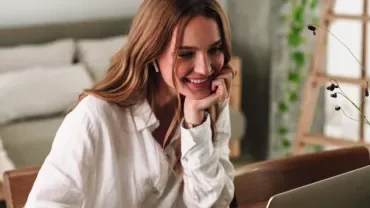 Woman smiling while using a laptop at a table.