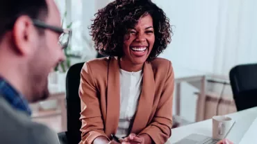 Three people laughing together in a bright office.