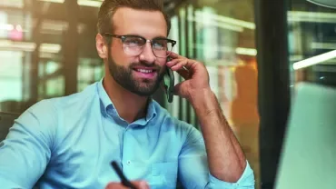 Man in office on phone, smiling at computer.