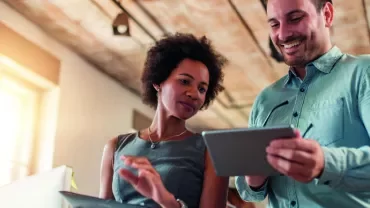Two colleagues smiling and using digital tablets in a bright office.