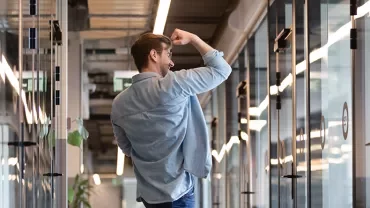 Man in hallway celebrating success with a fist pump.