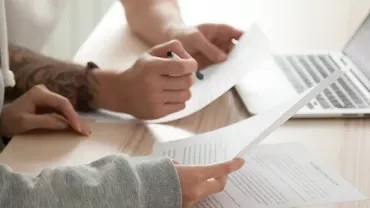 People reviewing documents at a desk with a laptop.