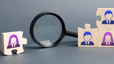 Wooden puzzle pieces with people icons and magnifying glass.