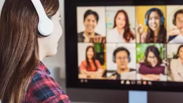 Person in headphones on a video conference with eight participants on a screen.