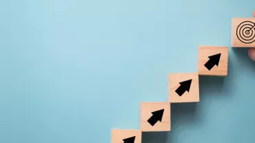 Hand placing target block after steps with arrows, blue background.
