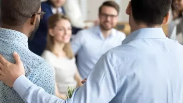Two men in a meeting room with people in the background.