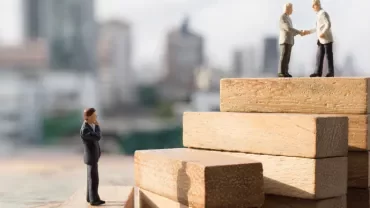 Miniature figures on wooden blocks, two shaking hands.
