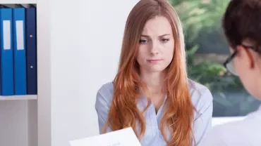 Two women at a desk, one looks concerned.