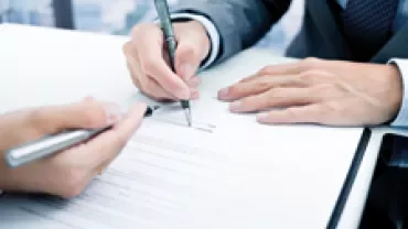 Two people signing documents at a desk.