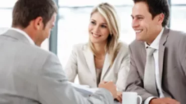 Three people in business attire having a meeting with coffee.