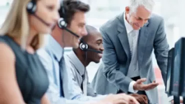 A business team with headsets working at computers, guided by a manager.