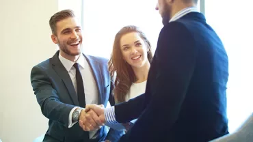 Three people in business attire smiling and shaking hands.