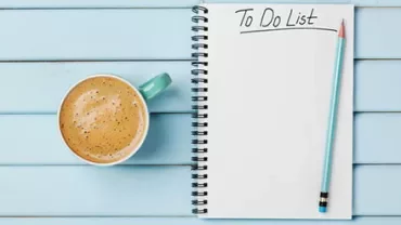 A to-do list on a notepad with a pencil and a cup of coffee on a blue wooden table.