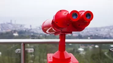 Red binocular telescope overlooking cityscape.