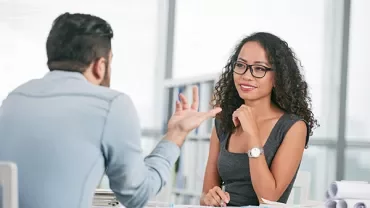 Two professionals having a discussion at a desk in an office setting.