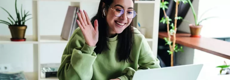 Person in green sweatshirt waving at a laptop during a video call.