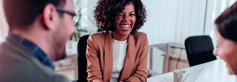 Three people laughing together in a bright office.