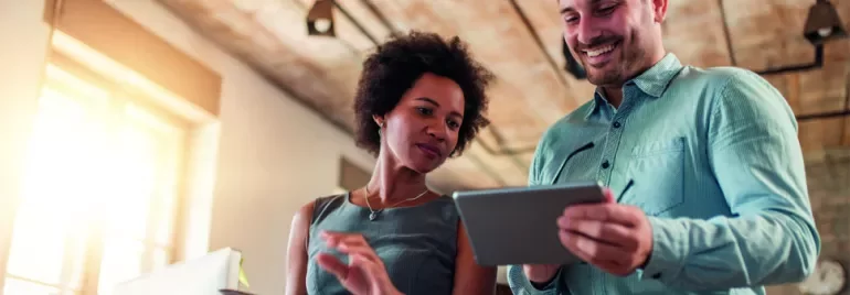 Two colleagues smiling and using digital tablets in a bright office.