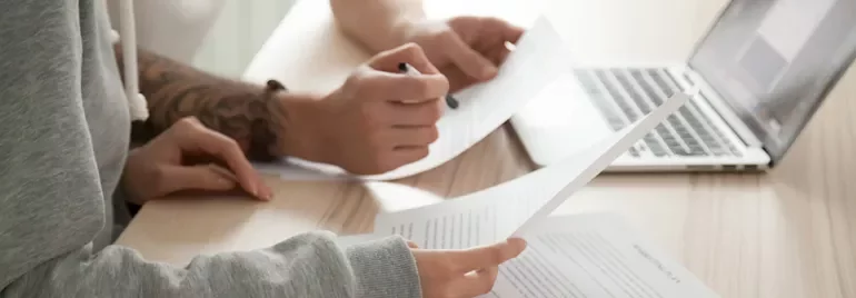 People reviewing documents at a desk with a laptop.
