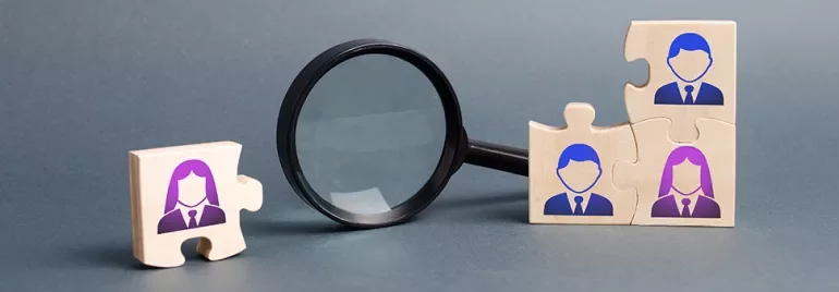 Wooden puzzle pieces with people icons and magnifying glass.