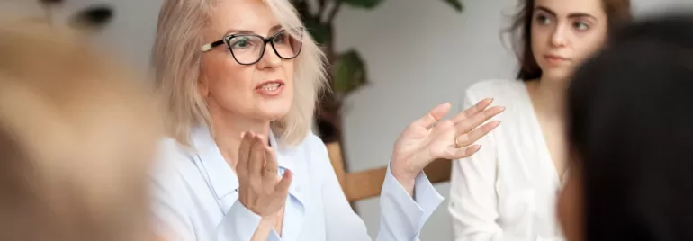 Older woman speaking in a meeting, while young woman listens attentively.