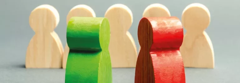 Two wooden figures, one green and one red, with four beige figures in the background.