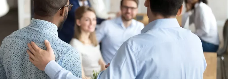 Two men in a meeting room with people in the background.
