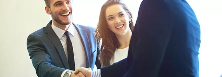 Three people in business attire smiling and shaking hands.