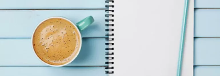 A to-do list on a notepad with a pencil and a cup of coffee on a blue wooden table.