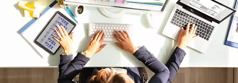 Person multitasking with tablet and laptop at desk
